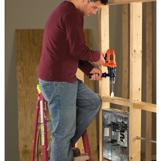 Photo of a person using BLACKDECKER DR560 electric drill on wood framing at construction site.