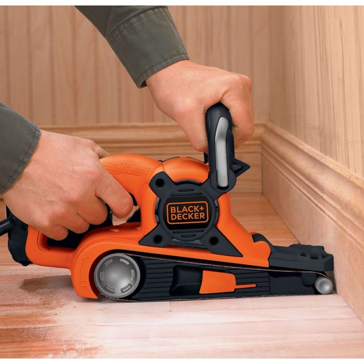 BLACKDECKER DS321 belt sander in use, close-up on wood floor near baseboard.