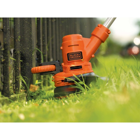 Photo of BLACKDECKER GH900 orange string trimmer cutting grass near a black fence.