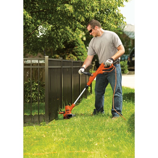 Photo of BLACKDECKER GH900 orange electric string trimmer used to edge grass along a metal fence outdoors.