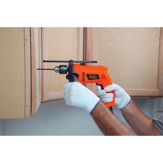 BLACKDECKER HD555 orange corded drill in use, drilling into wooden cabinet, user wearing white gloves.