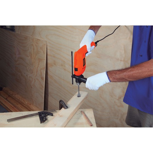 BLACKDECKER HD555 orange corded drill in use on wood, front angle, user wearing white gloves.