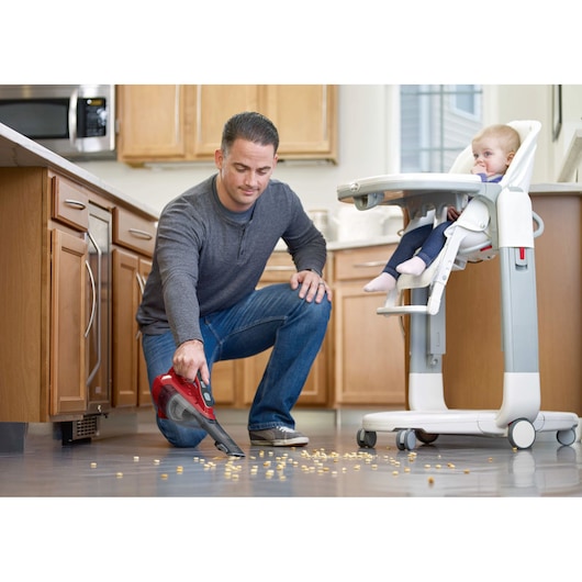 BLACKDECKER HLVA320J26 red handheld vacuum cleaner used to pick up crumbs from kitchen floor near high chair.