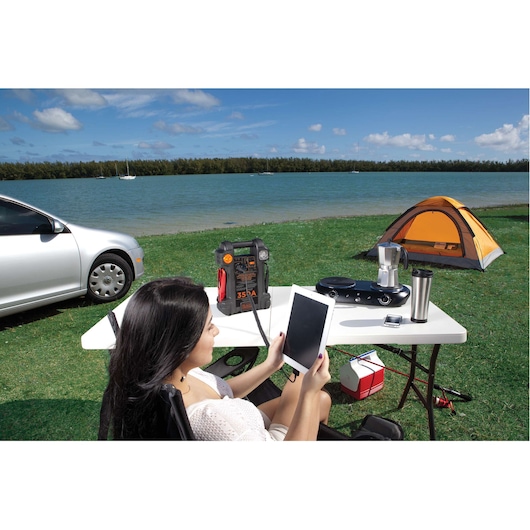 Photo of BLACKDECKER JS350CC portable jump starter on a picnic table at a lakeside campsite with camping gear.