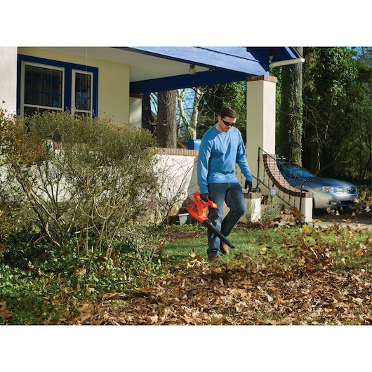 BLACKDECKER LB700 leaf blower in use outdoors, blowing leaves in front yard near bushes and house.