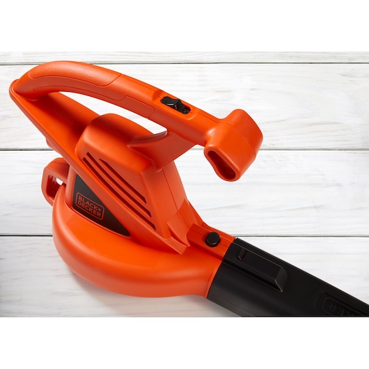 Photo of BLACK+DECKER LB700 leaf blower, orange and black, side view, white wood background.