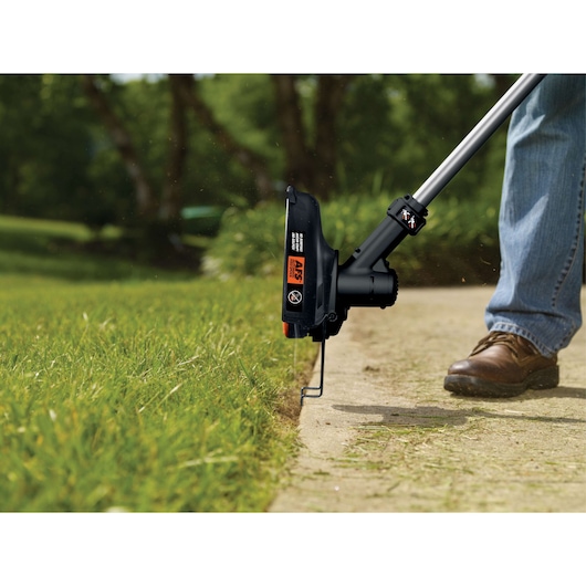 BLACKDECKER LST136 string trimmer in use edging grass along a sidewalk outdoors.