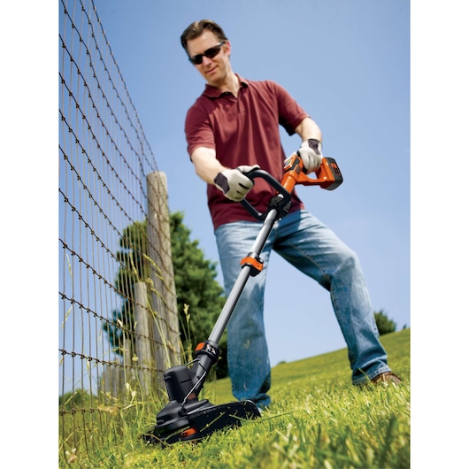 Photo of BLACKDECKER LST136 cordless string trimmer in use cutting grass near a wire fence outdoors.