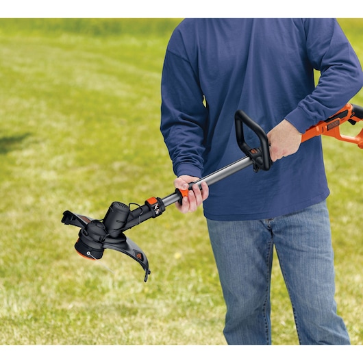 Photo of BLACK+DECKER LST136 string trimmer held by person outdoors on grass, showing orange and black design.