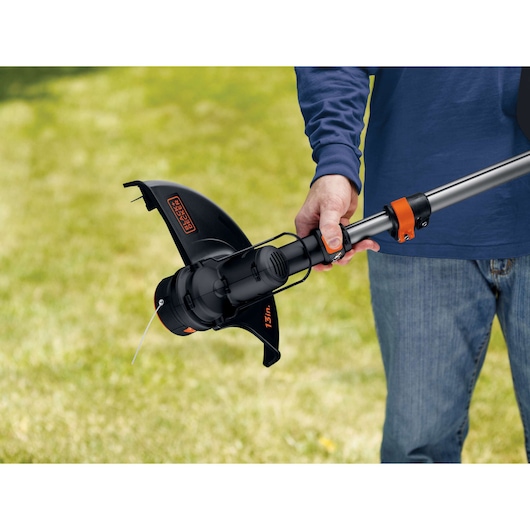 Photo of BLACKDECKER LST136 string trimmer being held in a person's hand, lawn background.