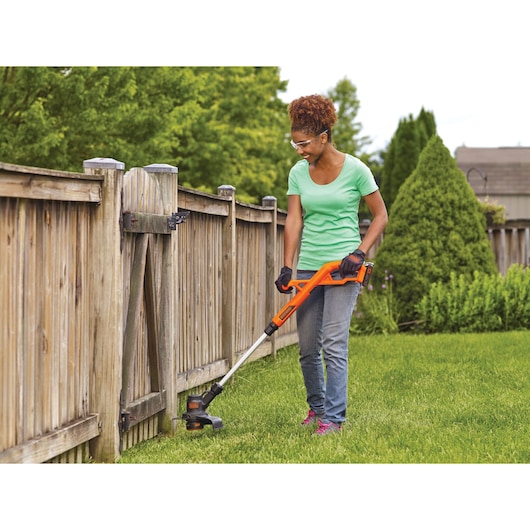 Photo of BLACKDECKER LST201 cordless string trimmer being used to edge grass near a wooden fence outdoors.