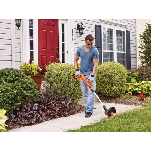 BLACKDECKER LST201 orange cordless string trimmer used to edge grass along a walkway in front of a house.