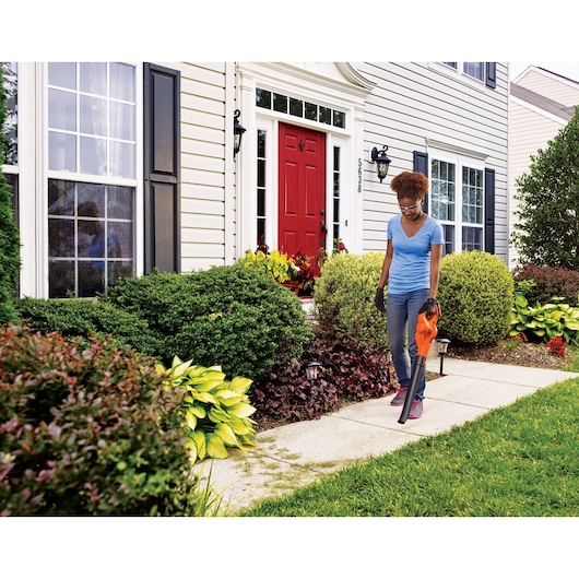 BLACKDECKER LSW221 cordless leaf blower used on sidewalk in front yard, home exterior visible.