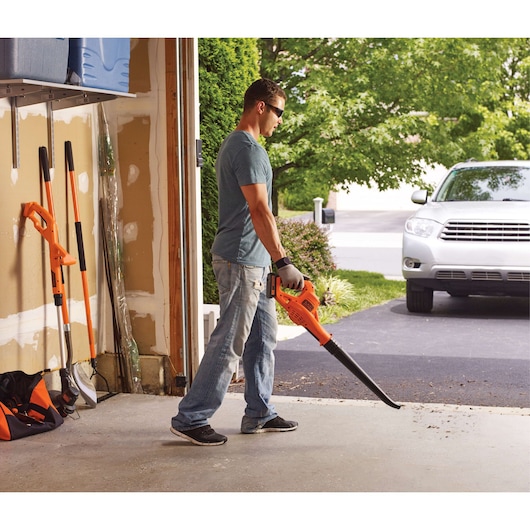 BLACKDECKER LSW221 cordless leaf blower used in garage and driveway, bright orange design, side angle
