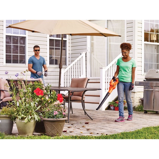 BLACKDECKER LSW221 cordless leaf blower in use on patio with plants and outdoor furniture.