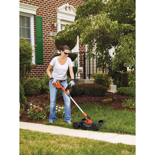 Photo of BLACKDECKER MTC220 lawn mower in use on grass, orange and black color, garden and sidewalk visible.