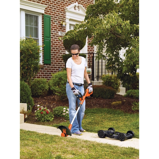 Photo of BLACKDECKER MTC220 trimmer and mower used outdoors on lawn near sidewalk, orange and black color.