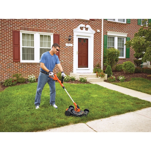 Photo of BLACKDECKER MTC220 lawn mower in use on grass by a person in front of a brick house.