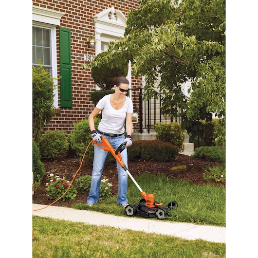 BLACKDECKER MTE912 corded lawn mower in use on grass near a sidewalk outside a brick house.