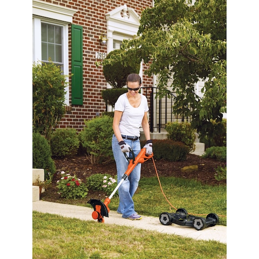 BLACKDECKER MTE912 corded lawn trimmer used outdoors near a garden sidewalk with orange and black design.