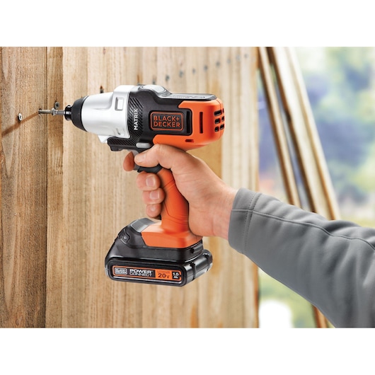 BLACKDECKER MTX20K6A cordless drill in use, orange and black, held against wooden wall.