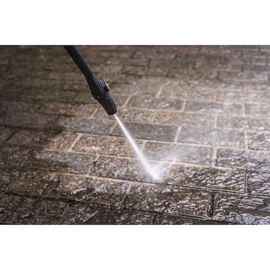 BLACKDECKER PW1450TD pressure washer spraying water on wet stone pavement, close-up photography.