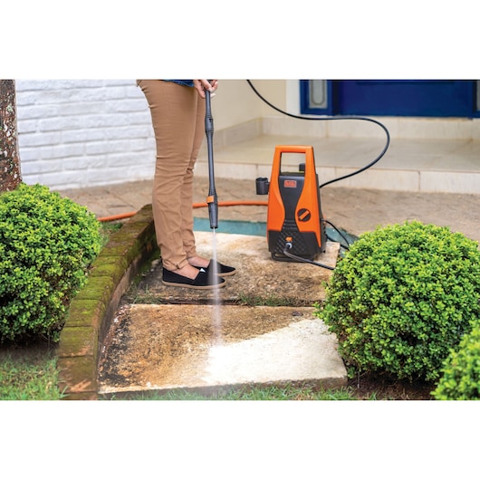 BLACKDECKER PW1450TD pressure washer cleaning outdoor stone path, orange and black unit shown.