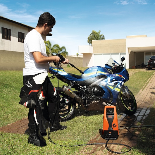 BLACKDECKER PW1450TD pressure washer being used to clean a blue motorcycle outdoors on a brick driveway.