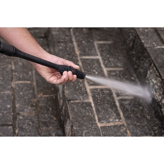 BLACKDECKER PW1450TD pressure washer spraying water on outdoor stone steps, close-up of nozzle in use.