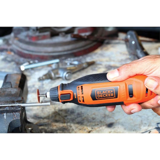 BLACK+DECKER RT18KA rotary tool in use, orange and black grip with cutting disc, workshop background.