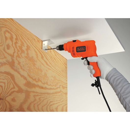 BLACKDECKER TP555 corded orange drill in use drilling metal bracket on wood panel close-up.